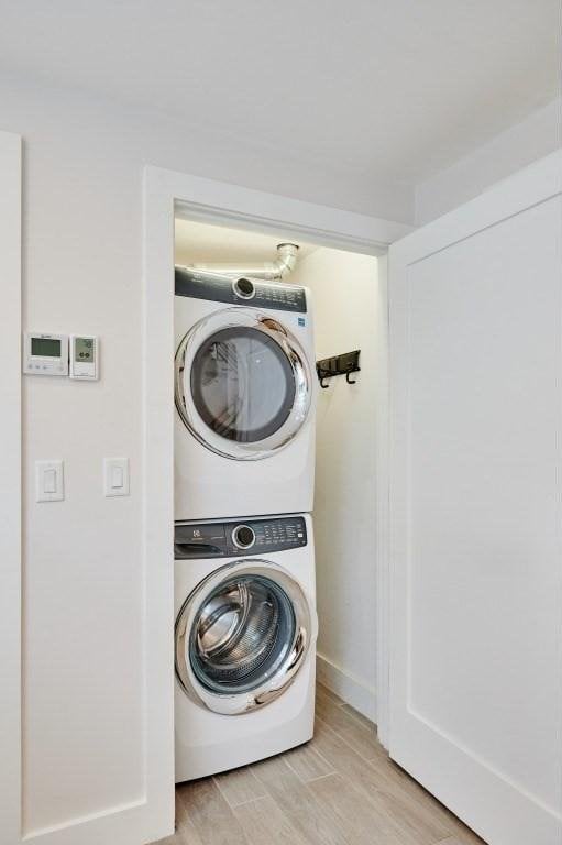 laundry area with light wood-type flooring, stacked washer and clothes dryer, baseboards, and laundry area