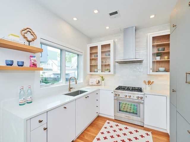 kitchen with a sink, visible vents, light countertops, high end stainless steel range oven, and wall chimney exhaust hood