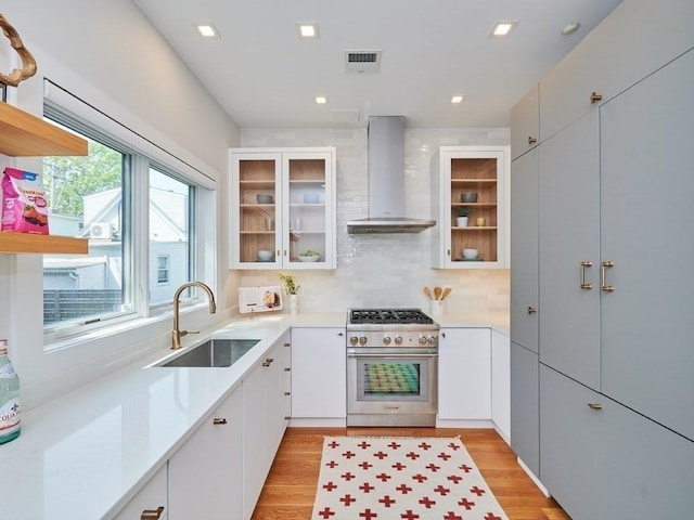 kitchen featuring high end stove, a sink, visible vents, light countertops, and wall chimney range hood