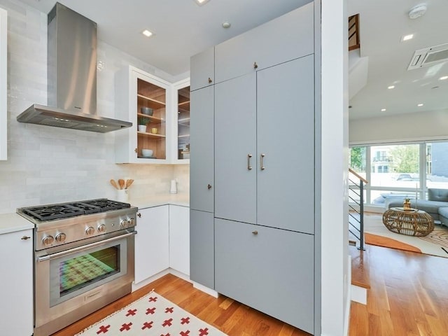 kitchen featuring high end stove, light wood-style floors, wall chimney exhaust hood, and light countertops