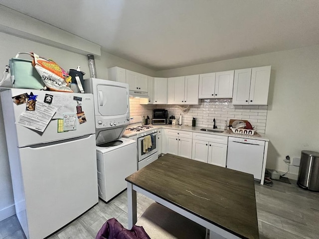 kitchen featuring decorative backsplash, white appliances, sink, stacked washer / dryer, and white cabinetry