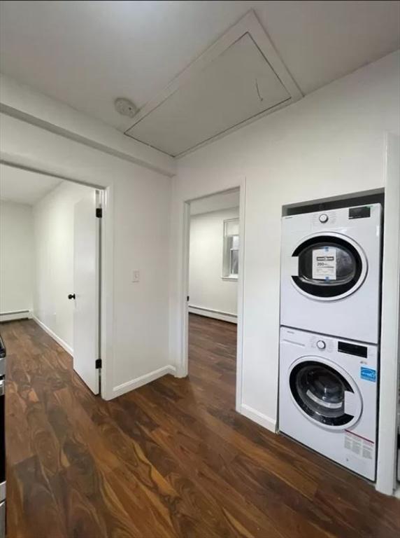 laundry room featuring a baseboard heating unit, dark wood-type flooring, and stacked washer / drying machine