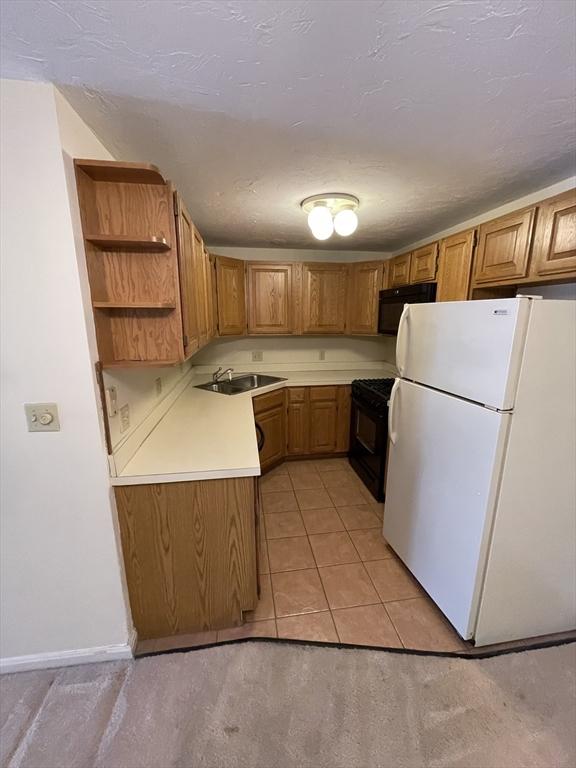 kitchen with a sink, light countertops, freestanding refrigerator, brown cabinets, and gas stove