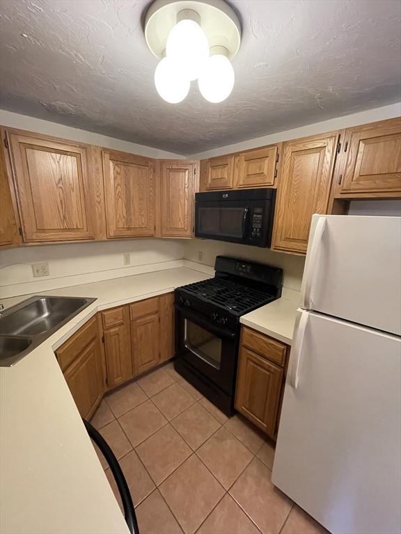 kitchen featuring light tile patterned floors, light countertops, a sink, a textured ceiling, and black appliances