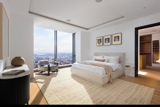 bedroom with floor to ceiling windows, light hardwood / wood-style floors, and a tray ceiling