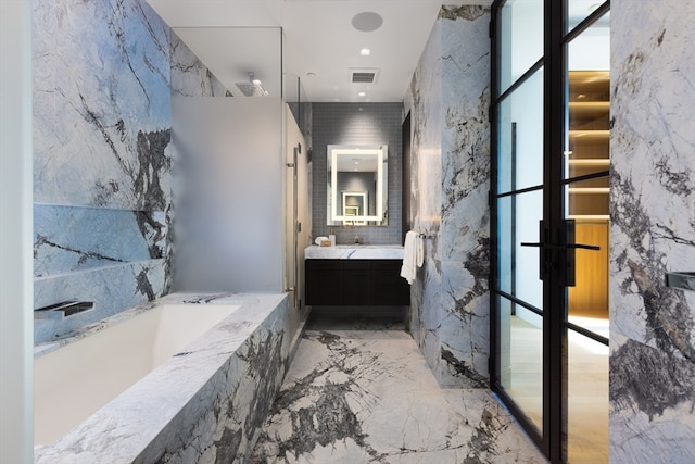 bathroom featuring vanity, tiled bath, a wealth of natural light, and tile walls