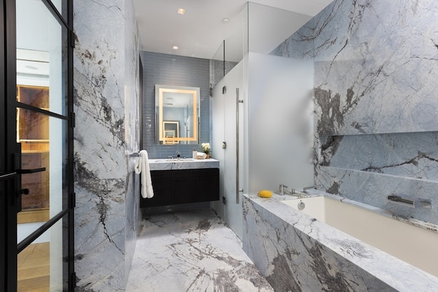 bathroom with tiled bath, tile walls, large vanity, and tile floors