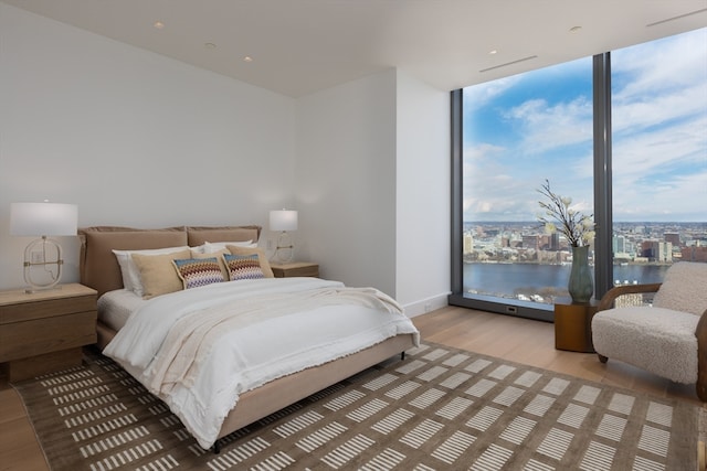 bedroom with a water view, light wood-type flooring, and a wall of windows