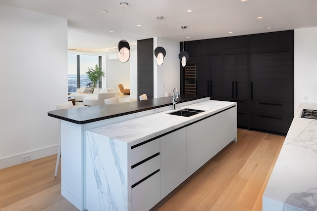 kitchen featuring sink, white cabinets, a center island with sink, decorative light fixtures, and light wood-type flooring