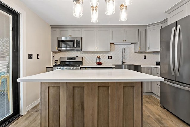 kitchen with appliances with stainless steel finishes, decorative light fixtures, sink, a center island, and light wood-type flooring