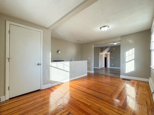 empty room featuring beamed ceiling, hardwood / wood-style floors, a textured ceiling, and baseboard heating