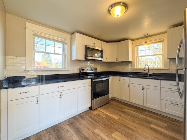 kitchen with sink, appliances with stainless steel finishes, white cabinets, decorative light fixtures, and light wood-type flooring