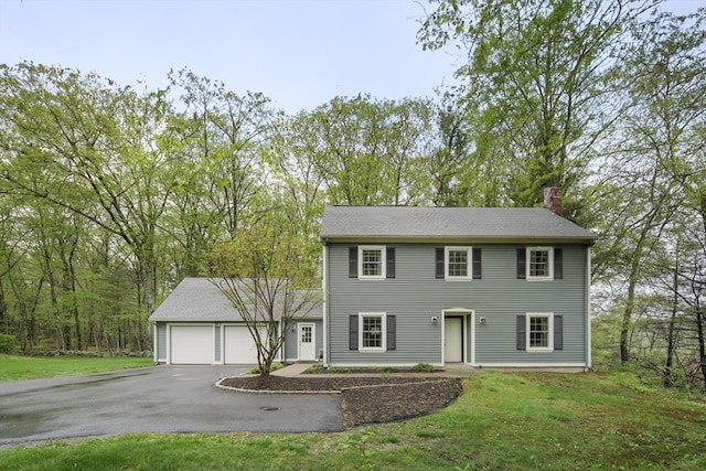 colonial inspired home with a chimney, asphalt driveway, an attached garage, and a front yard