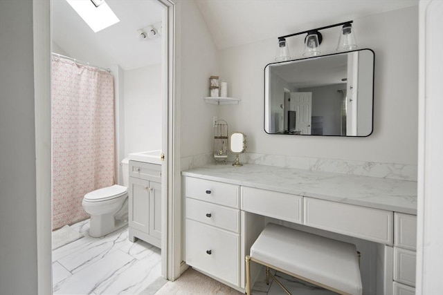 bathroom with marble finish floors, a skylight, vanity, vaulted ceiling, and toilet