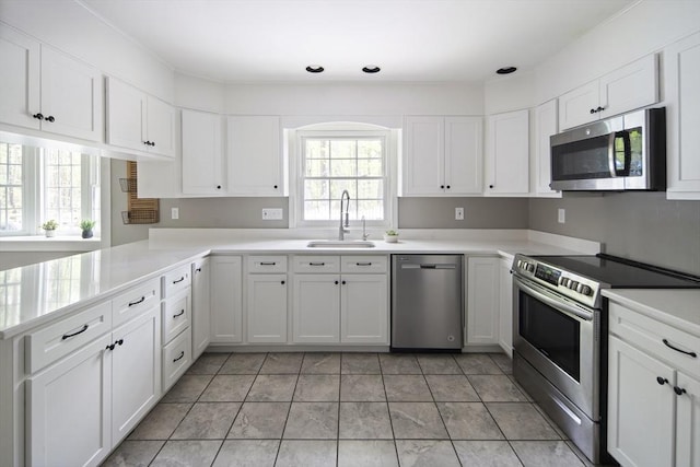 kitchen with stainless steel appliances, a sink, white cabinets, light countertops, and a peninsula