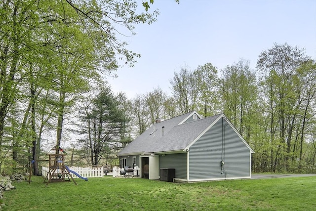 rear view of house featuring a playground, a yard, a shingled roof, and central air condition unit