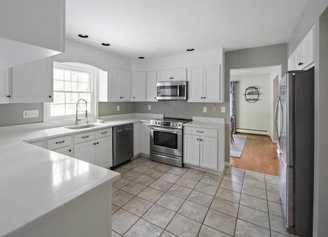 kitchen with stainless steel appliances, a sink, light tile patterned floors, baseboard heating, and white cabinets