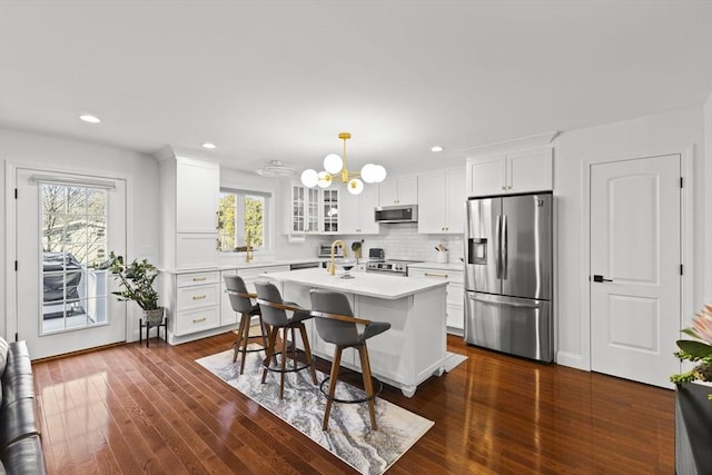 kitchen with white cabinetry, stainless steel appliances, an island with sink, hanging light fixtures, and a breakfast bar