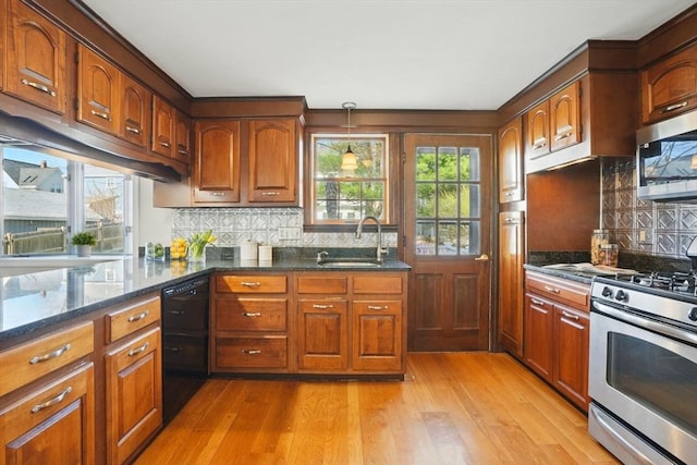 kitchen with brown cabinets, a sink, light wood-style floors, dark stone counters, and stainless steel appliances