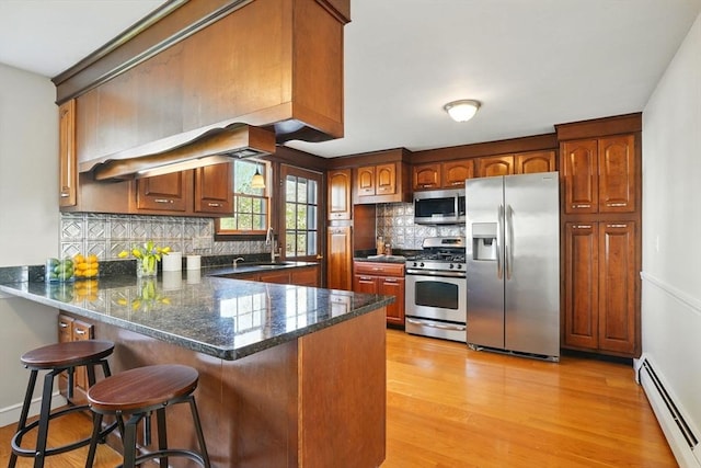 kitchen with a peninsula, light wood-style floors, a baseboard heating unit, tasteful backsplash, and stainless steel appliances