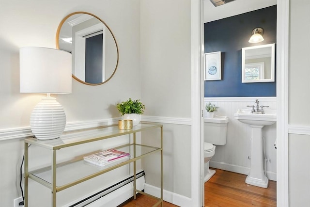 half bath with wood finished floors, toilet, and a wainscoted wall