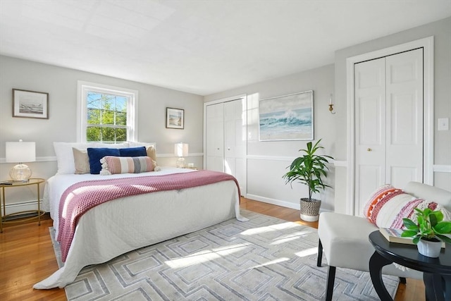 bedroom with baseboards, two closets, and wood finished floors