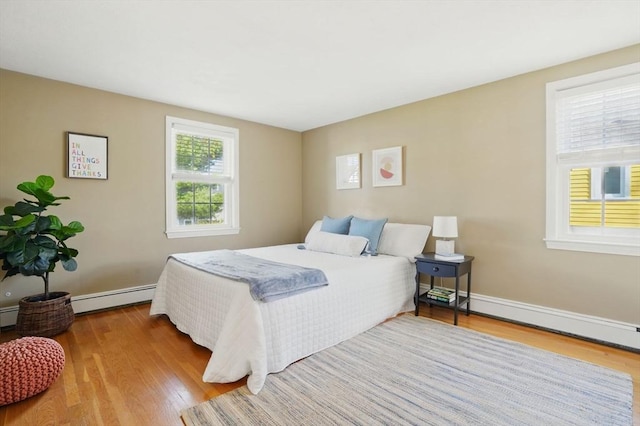 bedroom with baseboards, a baseboard heating unit, wood finished floors, and a baseboard radiator