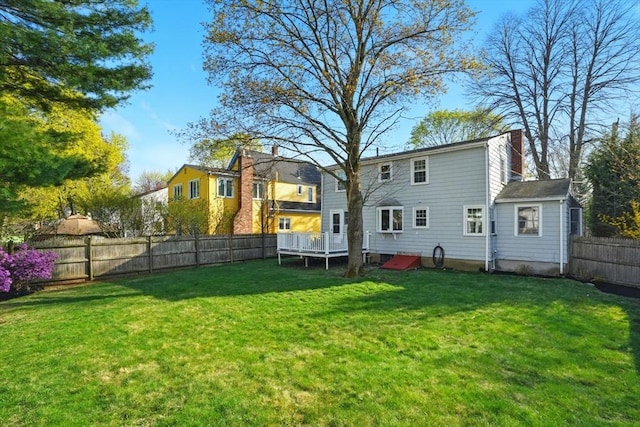 rear view of house with a fenced backyard, a yard, a chimney, and a deck