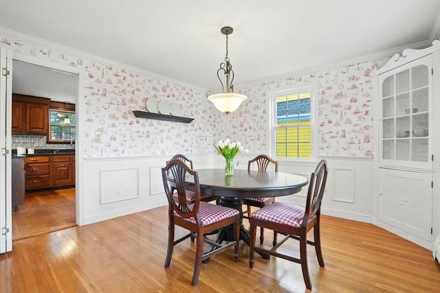 dining space featuring light wood-style floors, wainscoting, and wallpapered walls