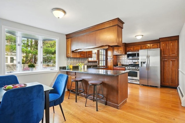 kitchen with appliances with stainless steel finishes, a breakfast bar area, a peninsula, decorative backsplash, and light wood-type flooring