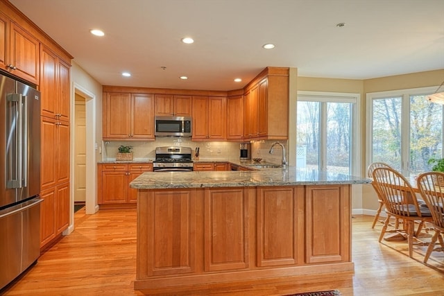 kitchen with kitchen peninsula, appliances with stainless steel finishes, light wood-type flooring, and light stone counters