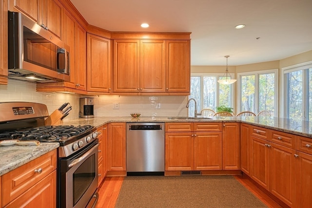 kitchen featuring light stone counters, stainless steel appliances, light hardwood / wood-style flooring, and sink