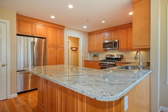 kitchen featuring sink, light stone counters, light hardwood / wood-style flooring, kitchen peninsula, and appliances with stainless steel finishes