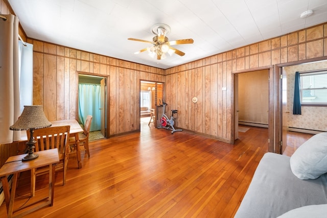 living area featuring hardwood / wood-style floors, ceiling fan, wood walls, and a baseboard heating unit