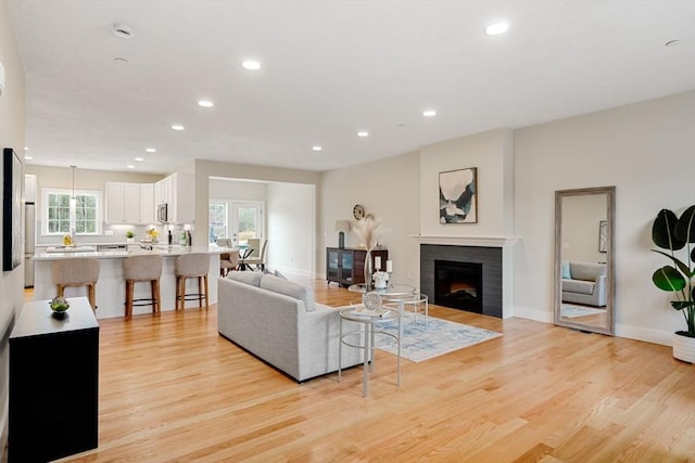 living room with light wood-type flooring, a wealth of natural light, and a tiled fireplace