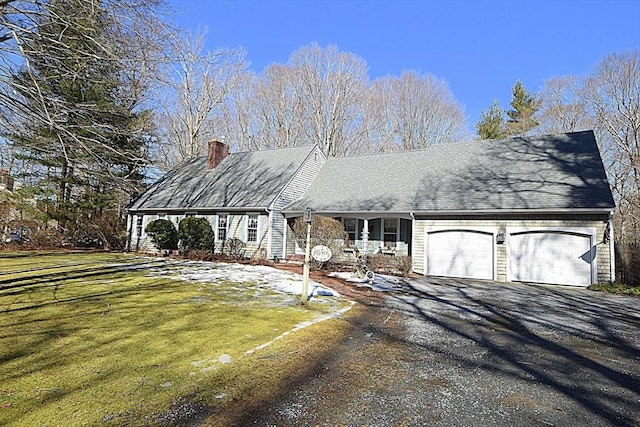 new england style home with a porch, a garage, driveway, a chimney, and a front yard