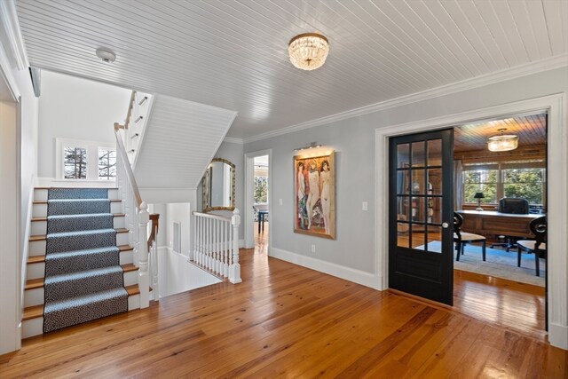 entrance foyer featuring an inviting chandelier, light hardwood / wood-style floors, wooden ceiling, french doors, and ornamental molding