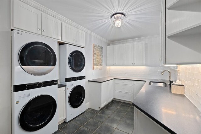 clothes washing area with dark tile floors, stacked washing maching and dryer, ornamental molding, and sink