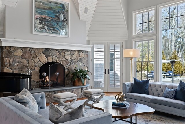 sunroom / solarium featuring a stone fireplace, vaulted ceiling, and french doors