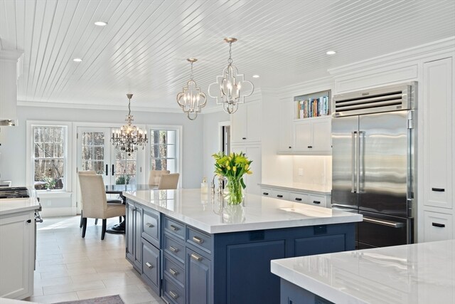 kitchen featuring pendant lighting, stainless steel built in fridge, white cabinetry, and a chandelier