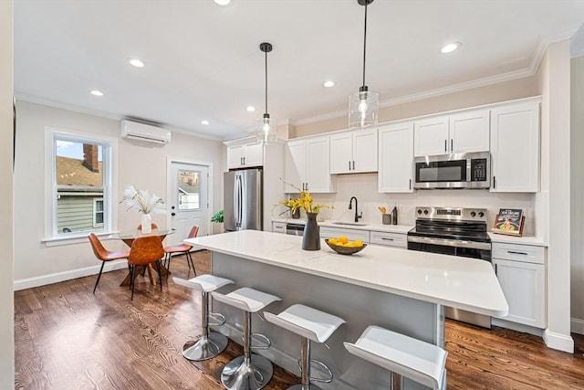 kitchen featuring a wall mounted air conditioner, a center island, hanging light fixtures, white cabinetry, and stainless steel appliances