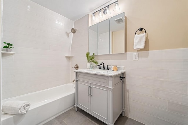 bathroom with tile patterned flooring, vanity, tile walls, and tiled shower / bath