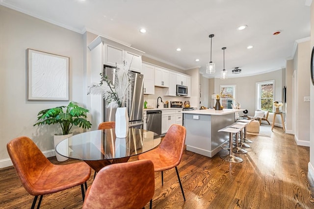 kitchen featuring appliances with stainless steel finishes, ornamental molding, pendant lighting, white cabinets, and a center island