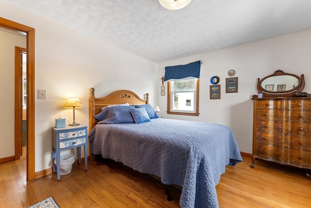 bedroom with a textured ceiling, hardwood / wood-style flooring, and baseboards