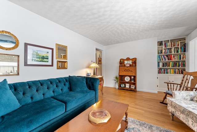 living room featuring built in shelves, a textured ceiling, baseboards, and wood finished floors