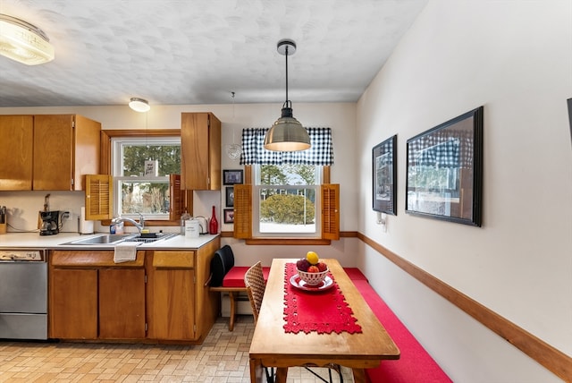 kitchen with pendant lighting, light countertops, brown cabinetry, a sink, and dishwasher