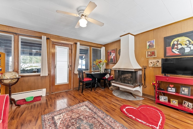 living room with a wood stove, wooden walls, baseboard heating, and wood finished floors