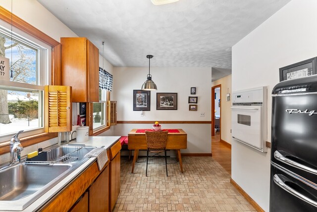 kitchen featuring white oven, brown cabinets, light countertops, hanging light fixtures, and a sink