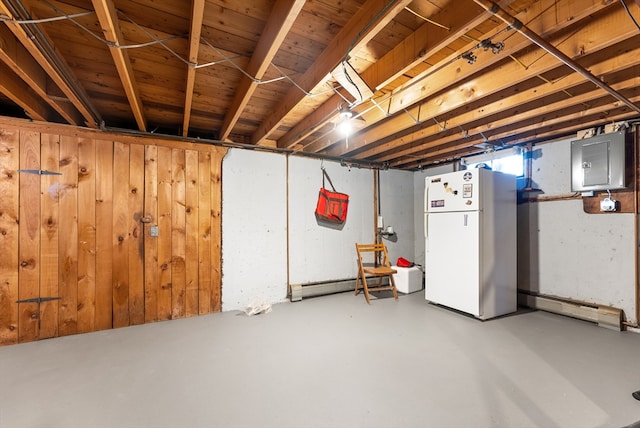 basement with wood walls, a baseboard radiator, electric panel, and freestanding refrigerator