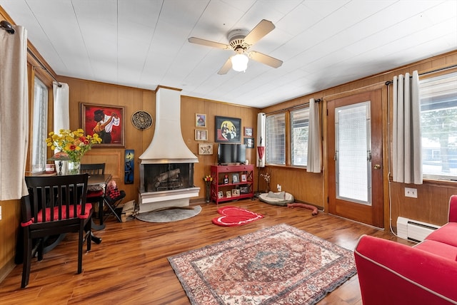 living room featuring a wood stove, wooden walls, a baseboard heating unit, and wood finished floors